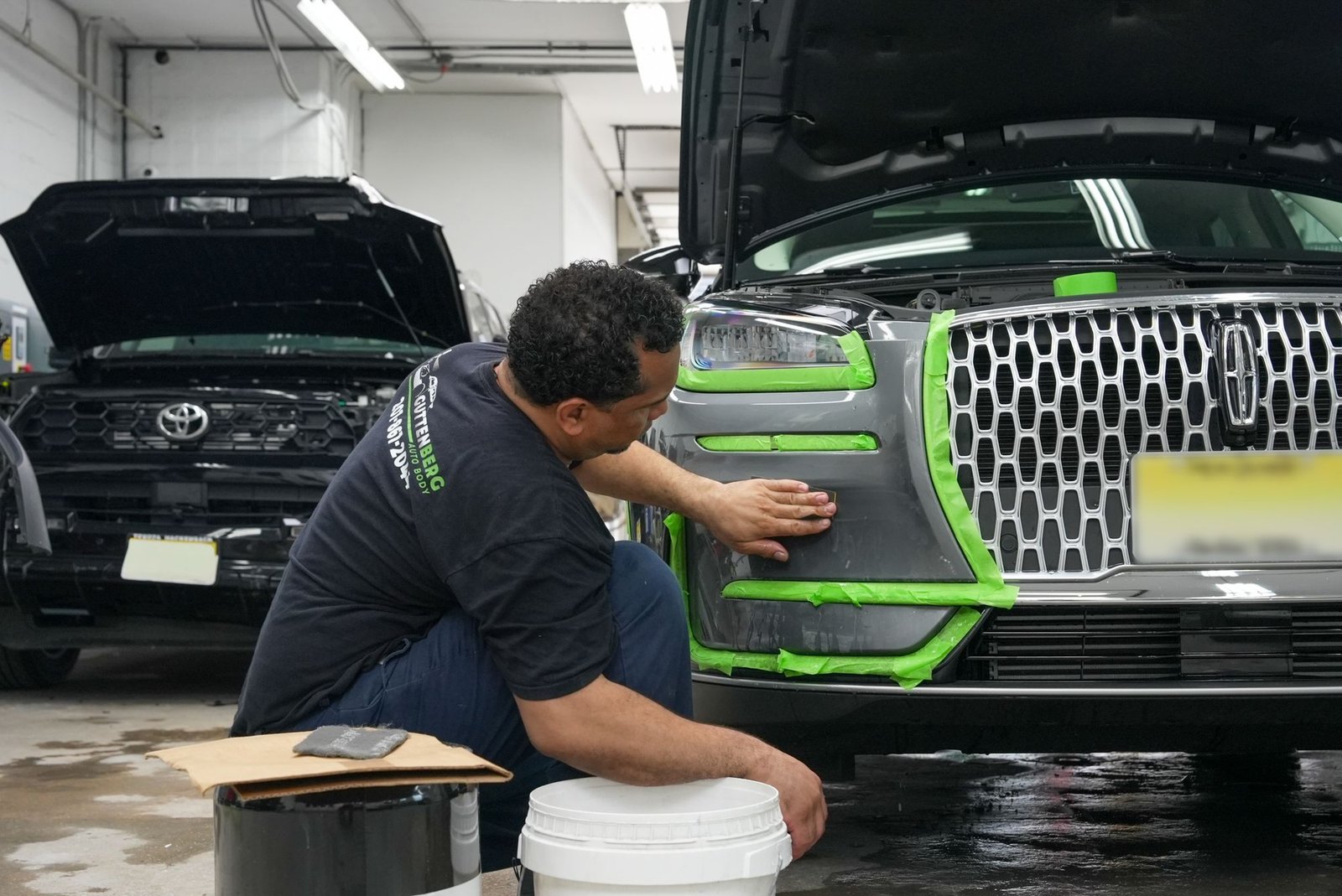 Technician prepping a masked front bumper for repair at Guttenberg Auto Body